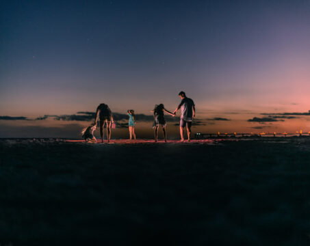 Five people standing on a beach at dusk, silhouetted against a colorful sunset sky.