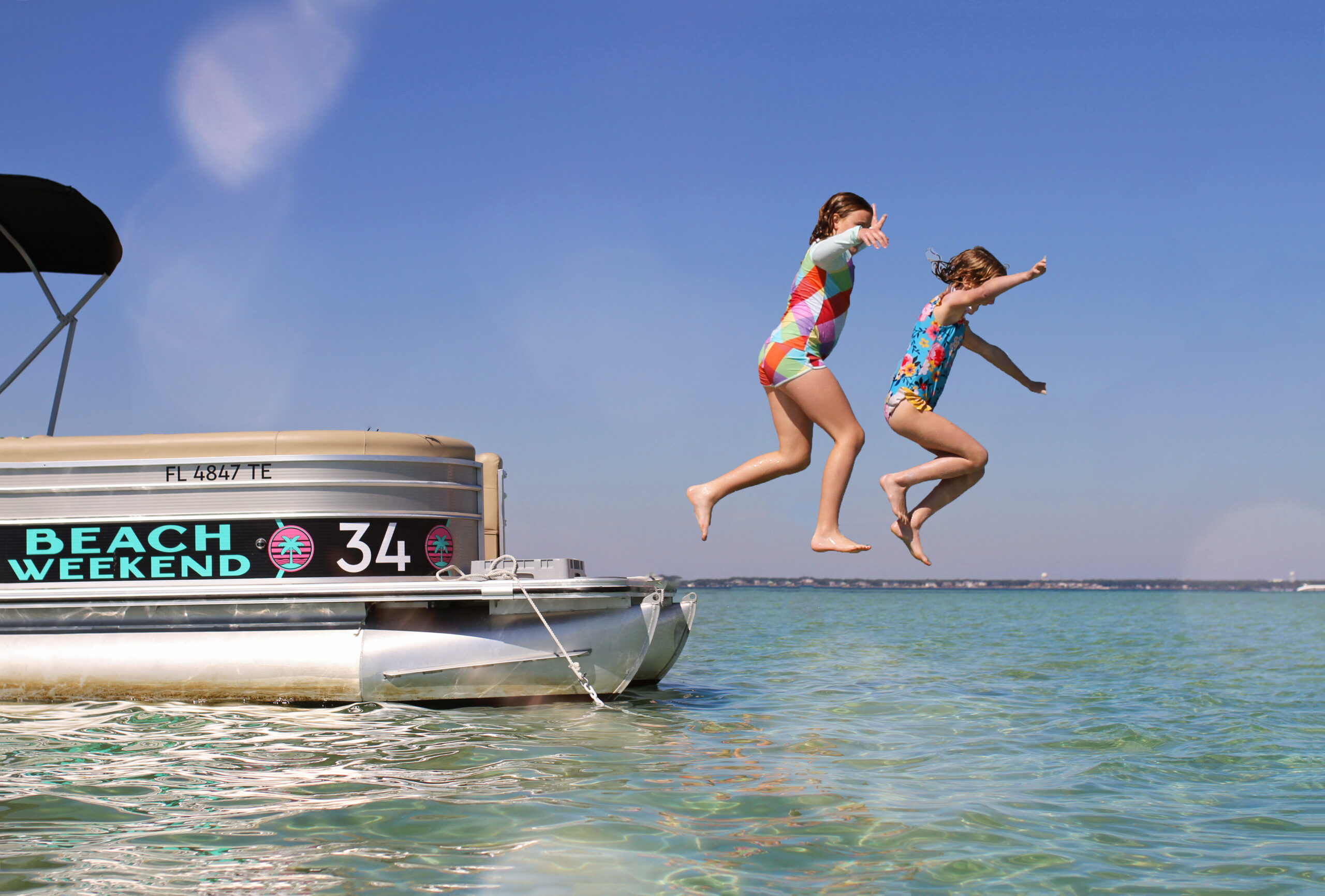 Two kids jumping into water from a pontoon boat