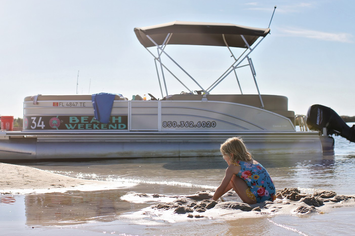 Kid digs in sand next to pontoon boat