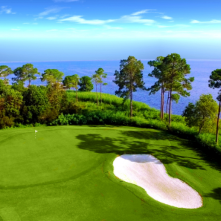 A golf course with a green sand bunker overlooking the ocean.