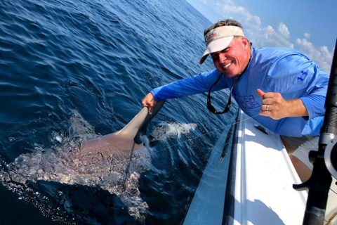 A man on a boat with a shark in the water.