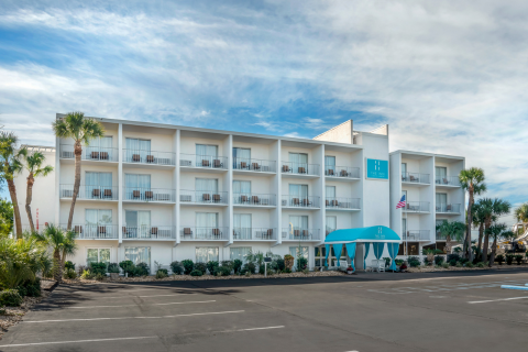 The front of a hotel with blue awnings and palm trees.