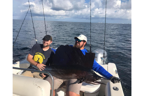 Two men on a boat holding a sailfish.