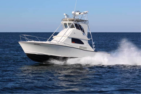 A white cabin cruiser boat speeding on the water with spray around the hull.