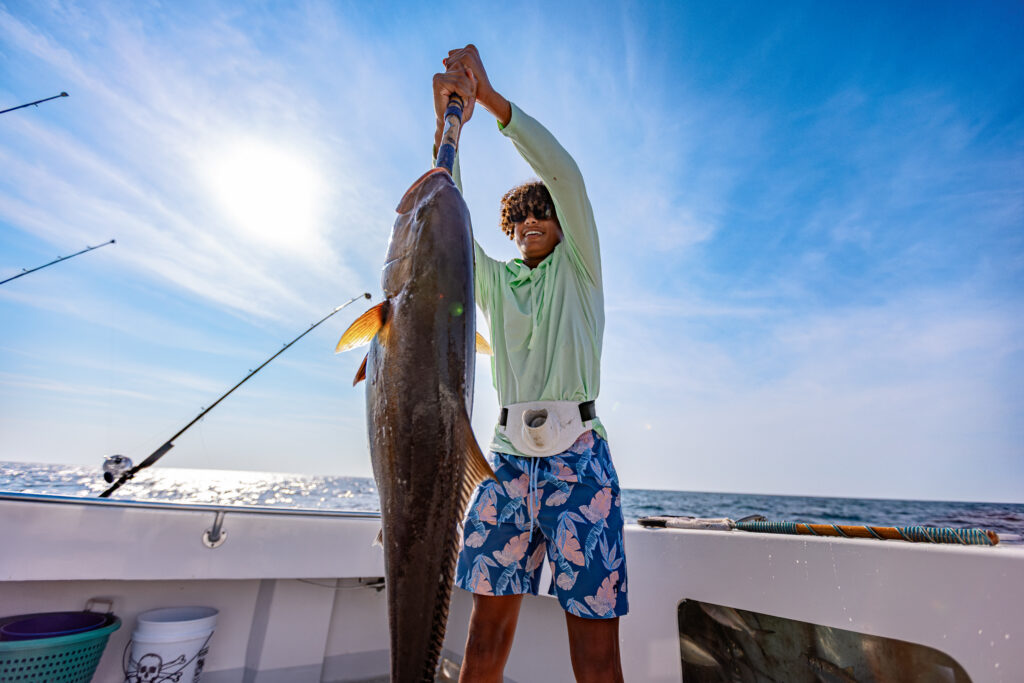 Teenage boy standing on boat in the gulf holding a large fish