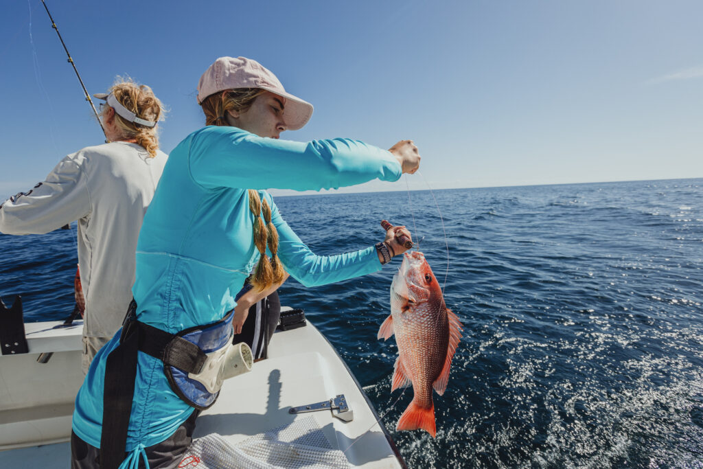 two people fishing on a boat in the ocean, one person caught a fish and is holding it up