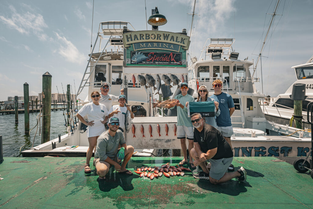 Group of people standing on a doc infront of a boat with fish laid out on the ground