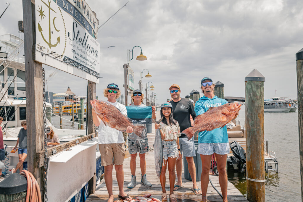Group of people standing on a dock holding fish they caught