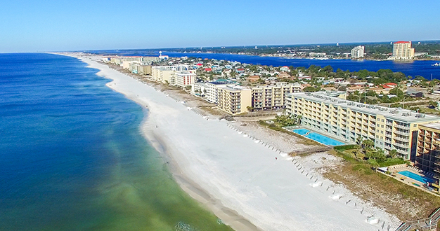 Aerial view of a coastal city with high-rise buildings, a sandy beach, and the ocean on one side and an inland waterway on the other.