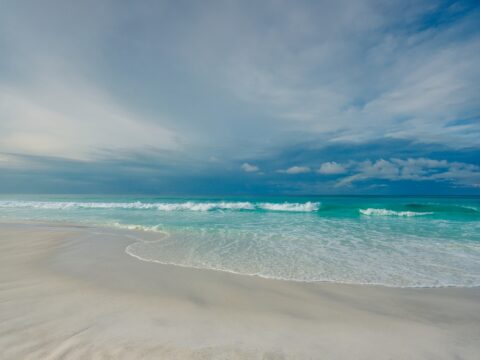 A serene beach scene with gentle waves lapping against the shore, under a cloudy sky.