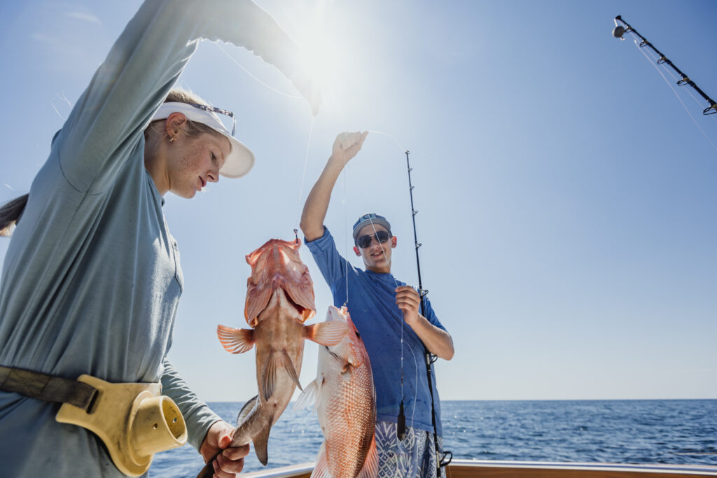Two people standing on a boat in the ocean holding up fish they caught