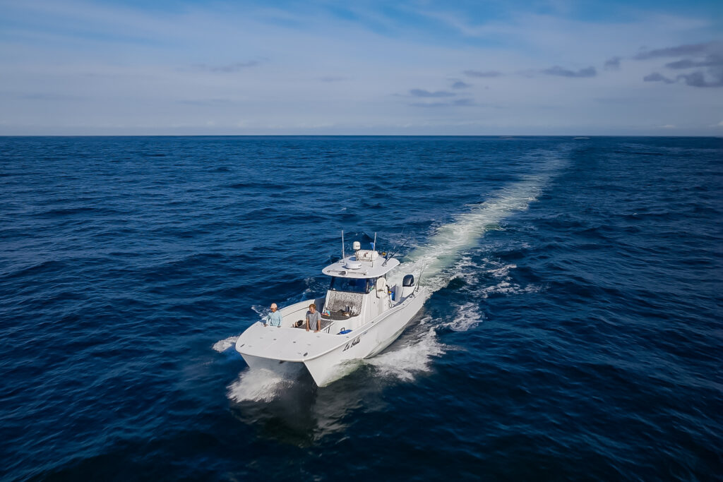 A white boat speeds across a deep blue ocean under a clear sky, leaving a white wake behind.