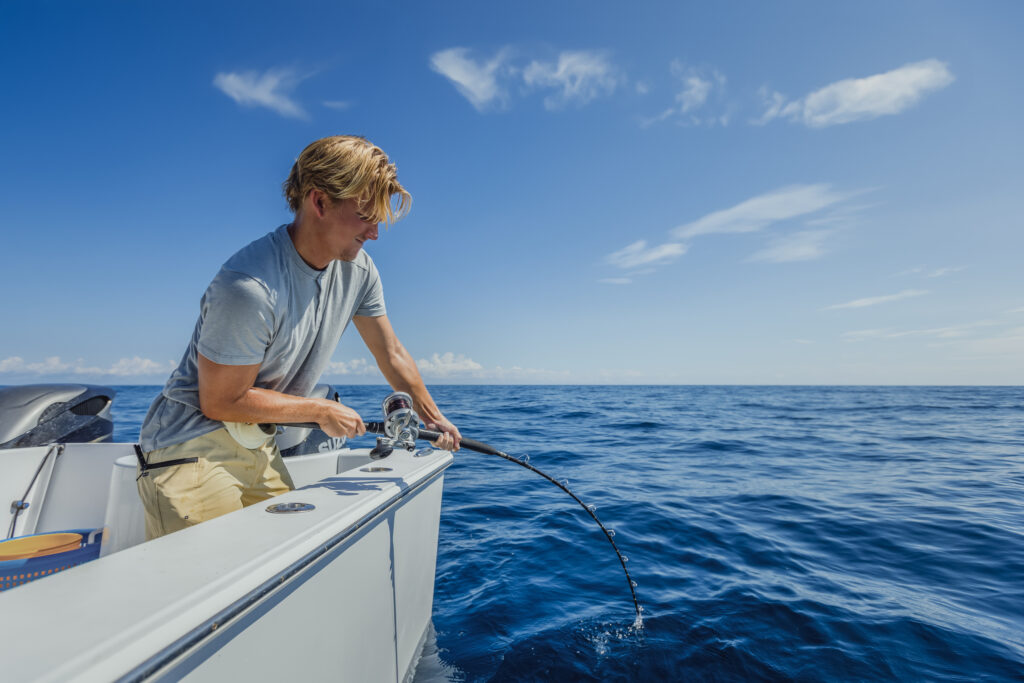 Person on a boat, fishing in open sea under a clear blue sky.