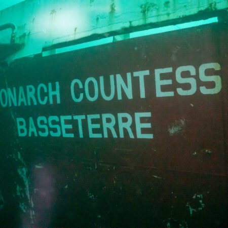A rusty, partially submerged ship hull with the words "MONARCH COUNTESS BASSETERRE" painted in white letters.