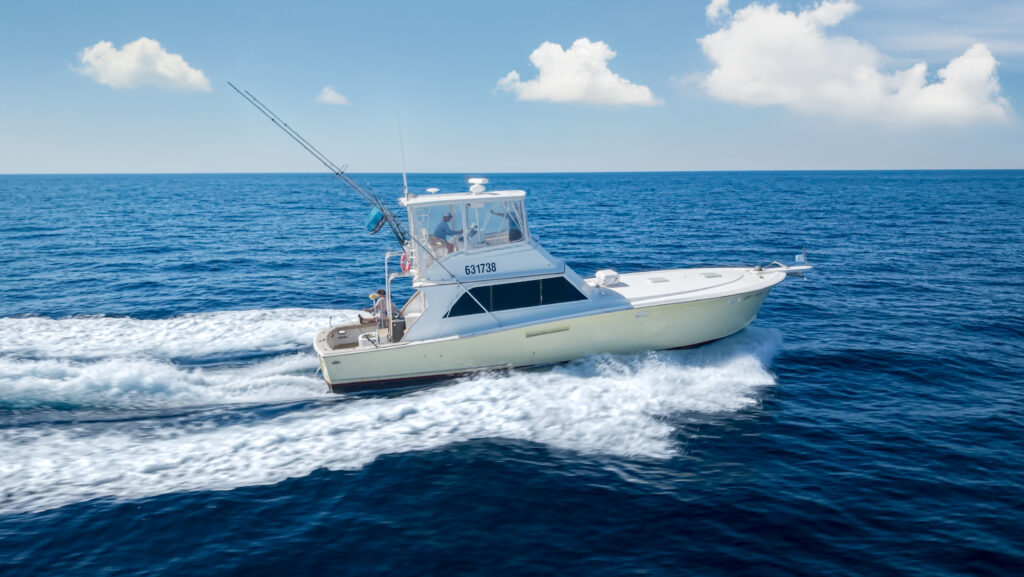 A white motor yacht cruises quickly across calm blue ocean water under a partly cloudy sky.