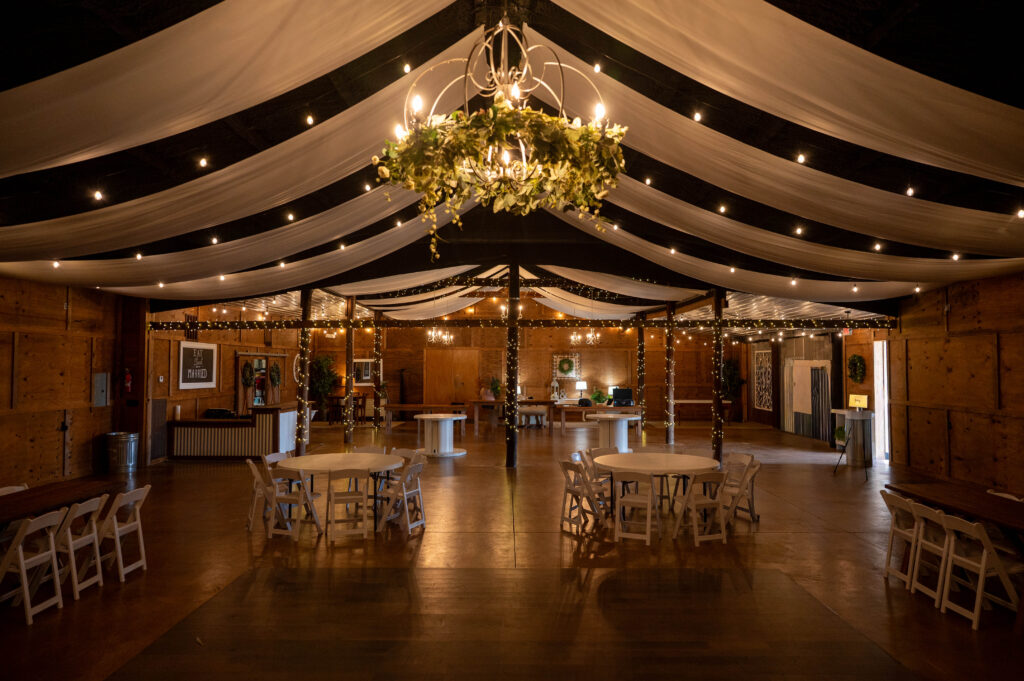Indoor barn wedding space with drapes on the ceiling and empty tables and chairs set up