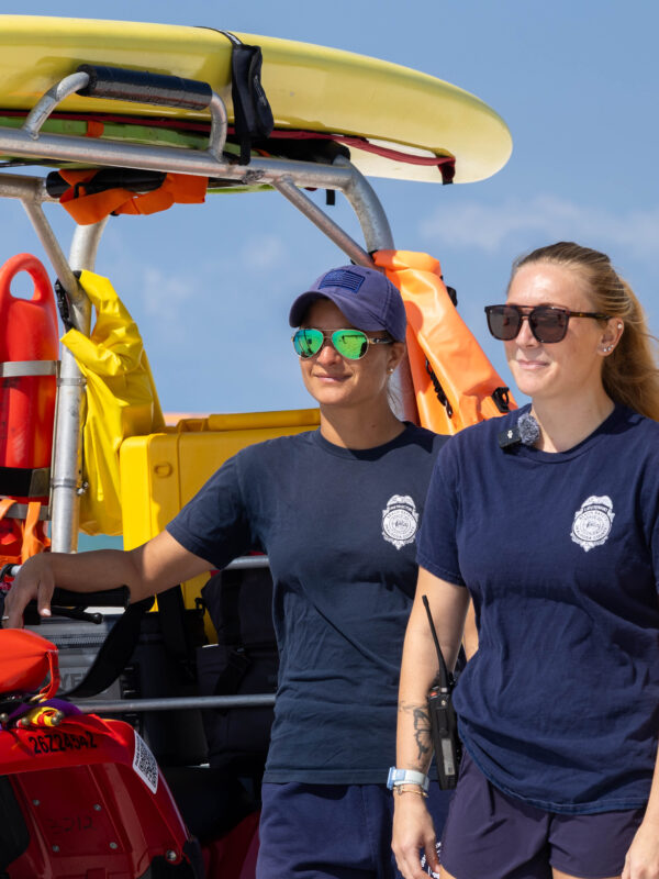 Two lifeguards standing in front of an ATV and standing at an Okaloosa Island beach.