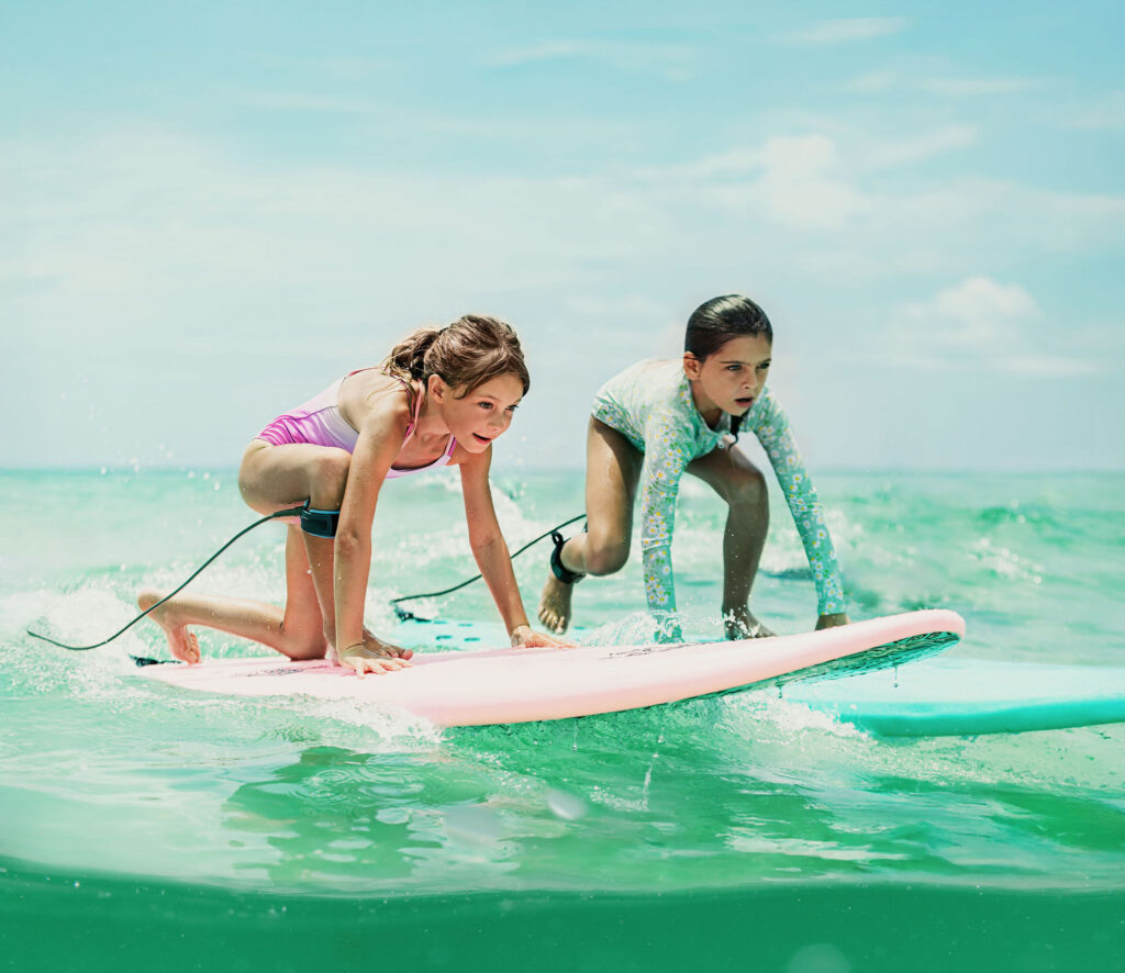 Two young girls stand up on surfboards in the ocean
