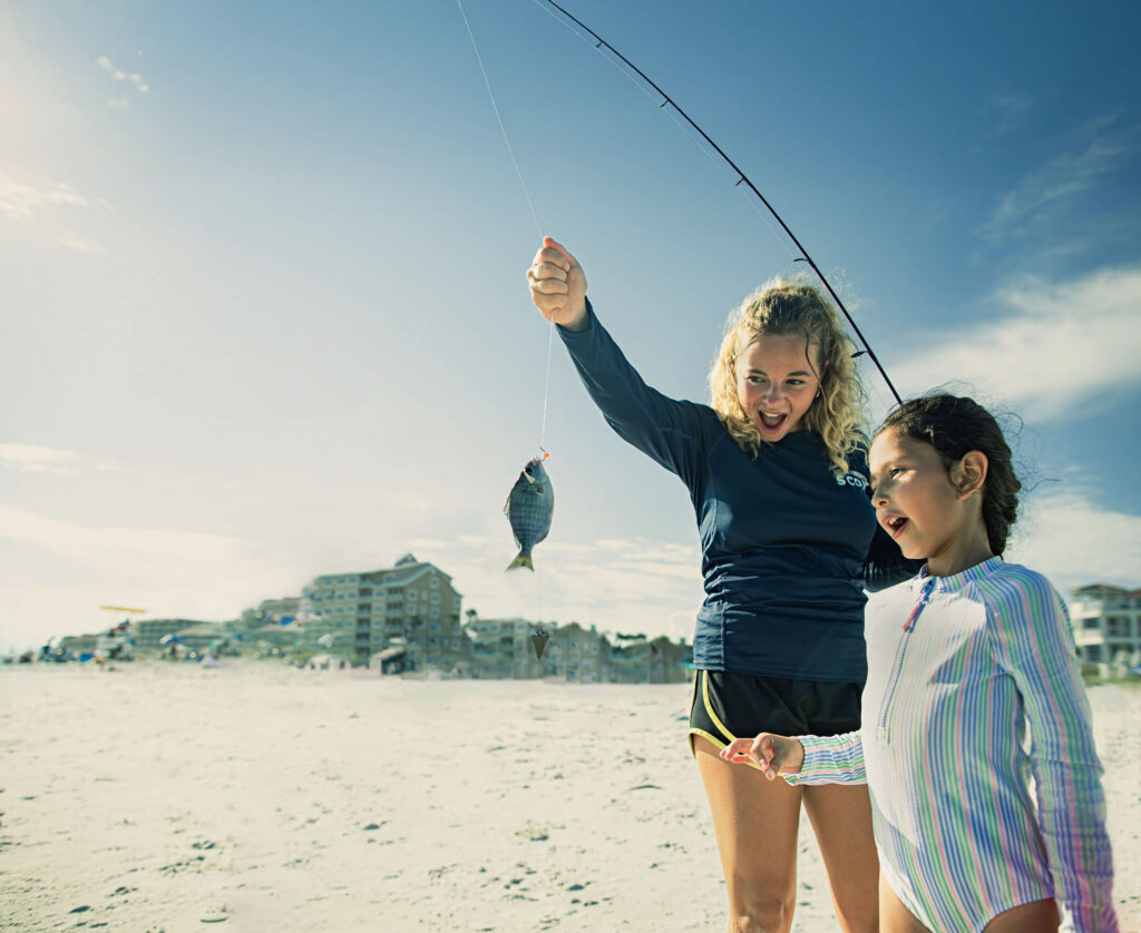 Two young kids look at a fish on the end of a fishing pole