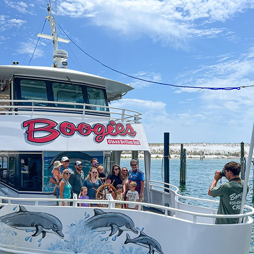 A group of people poses for a photo on the deck of a boat labeled &ldquo;Boogies Glass Bottom Boat&rdquo; while a photographer stands on the dock.